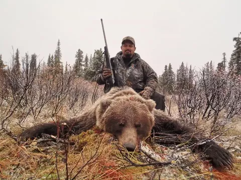 man holding rifle with bear kill