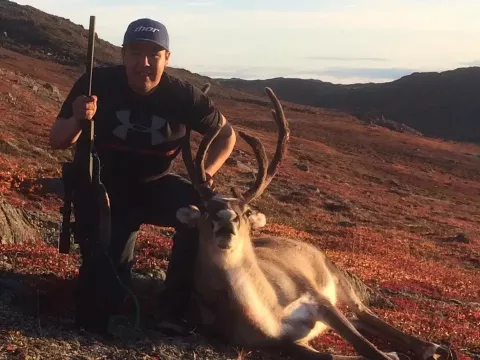 man holding rifle with caribou kill