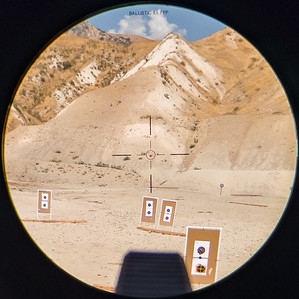 View through a scope at a ballistic reticle positioned over targets in the desert mountains