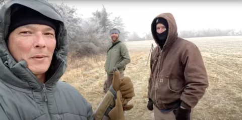 Three men in field on tree line in cold weather wearing jackets